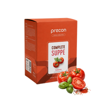Auf weißem Hintergrund ist eine rote Verpackung der „Complete Suppe Tomate“ von Anona GmbH neben frischen Tomaten, Basilikumblättern und Tomatenpulver abgebildet.